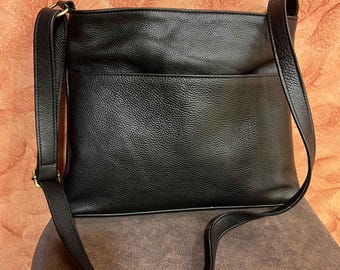 May include: Black crossbody bag with a textured finish. The bag has a rectangular shape with a front pocket and a long, adjustable strap. The bag is made of a leather-like material and has gold-coloured hardware.