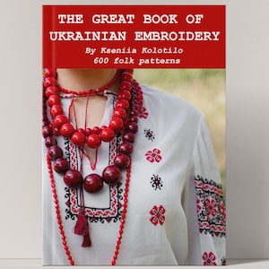 May include: A book titled "THE GREAT BOOK OF UKRAINIAN EMBROIDERY" with a red cover. The image shows a person wearing a white embroidered shirt and a red beaded necklace. The shirt has red and black floral embroidery.
