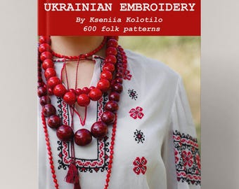 May include: A book titled "THE GREAT BOOK OF UKRAINIAN EMBROIDERY" with a red cover. The image shows a person wearing a white embroidered shirt and a red beaded necklace. The shirt has red and black floral embroidery.