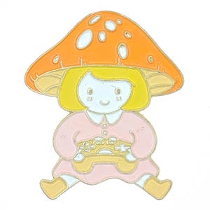 May include: A colorful enamel pin featuring a cartoon character with a mushroom cap. The character is wearing a pink dress and holding a yellow game controller. The mushroom cap is orange with white spots, and the character has yellow hair.