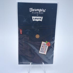 May include: A Farmgirl Flowers x Levi's pin featuring a denim jacket design. The pin includes the text "VOTE" in red and white, with a red flower accent. The packaging includes the Farmgirl Flowers and Levi's logos.