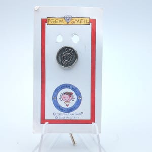 May include: A silver-colored pin with the letters "CTR" and a smiling face is displayed on a white card with red borders. The card also features the text "The Gem Smith" and a circular graphic with a cartoon girl and the words "Charmed by Amy Dott."