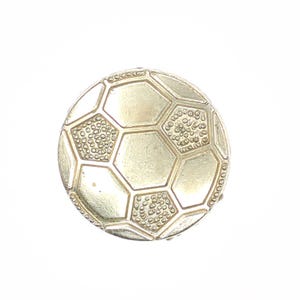 May include: A silver-colored soccer ball-shaped object. The ball is made of interlocking pentagons and hexagons, with textured details on some panels. The object is likely a decorative item or a piece of jewelry.