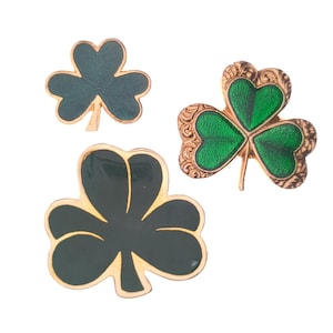 May include: Three shamrock brooches, one with a gold-tone finish and green enamel, and two with a black finish and green enamel.