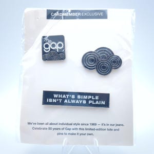 May include: A set of Gap pins, including a black square pin with the Gap logo and wave design, and a pin with the text "WHAT'S SIMPLE ISN'T ALWAYS PLAIN." The pins are packaged on a white card.