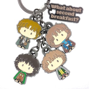 May include: A metal keychain featuring four chibi-style character charms and a rectangular charm with the text "What about second breakfast?" in a dark font. The characters have curly hair and wear detailed outfits in shades of green, brown, and blue.