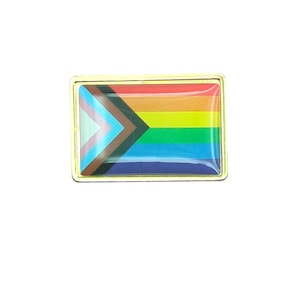 May include: A rectangular pin with a gold-colored border. The pin features a colorful design representing the Progress Pride flag. The flag design includes the traditional rainbow colors, along with additional stripes for transgender, Black, and brown communities.