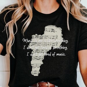 May include: Black t-shirt with a white graphic of music notes and the text "Music to me is like breathing. I don't get tired of breathing. I don't get tired of music."