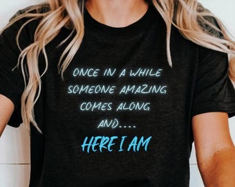 May include: Black t-shirt with the text "Once in a while someone amazing comes along and... Here I am" in blue.