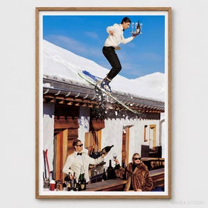 May include: A framed art print depicting a person in a white hoodie and black pants skiing off a snowy roof while holding a tray with a bottle and glasses. Below, a person in a white jacket pours wine while another in a fur coat sits nearby.