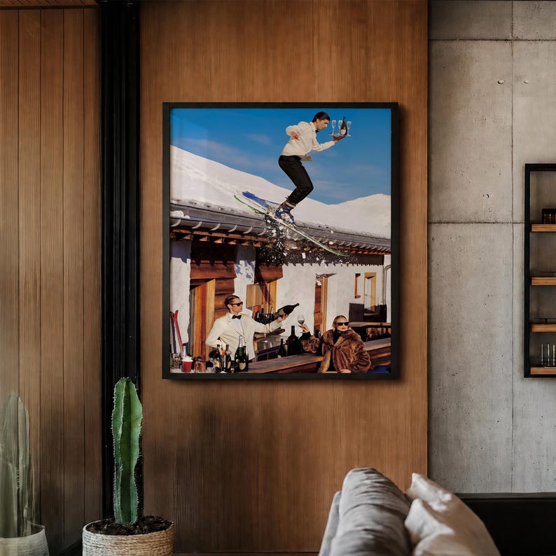 May include: A framed wall art print depicting a person in a white sweater and black pants skiing off a snowy roof while holding a tray with glasses, above two people at a bar counter, one in a white suit and one in a brown fur coat.