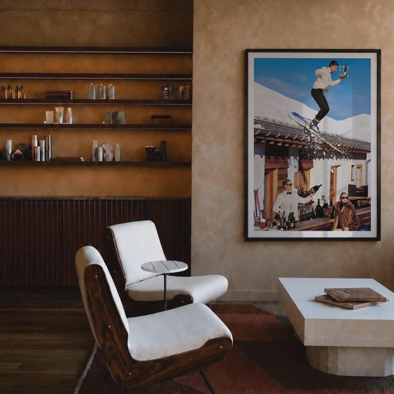 May include: A lounge area featuring two white upholstered chairs with dark wood frames, a small round side table, and a low white rectangular coffee table. A large framed photograph on the wall depicts a skier jumping over a building and a bar scene.