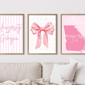 May include: Three framed prints with a pink theme. The left print has pink and white stripes and the text "University of Georgia". The centre print features a pink bow. The right print shows a pink outline of Georgia with the text "Athens, Georgia".