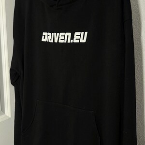 Peut inclure: Sweat-shirt &agrave; capuche noir avec un logo blanc qui dit "DRIVEN.EU"