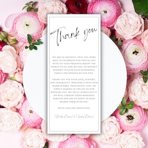 May include: A white thank you card with black text. The card reads "Thank you" in cursive and includes a message expressing gratitude for the recipient's presence at a wedding. The card is surrounded by pink flowers.