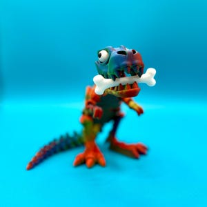 Puede incluir: Un juguete de dinosaurio colorido con un hueso en la boca. El dinosaurio está pintado con una mezcla de tonos rojos, naranjas, verdes y azules. El hueso es blanco. El juguete está sobre un fondo azul brillante.