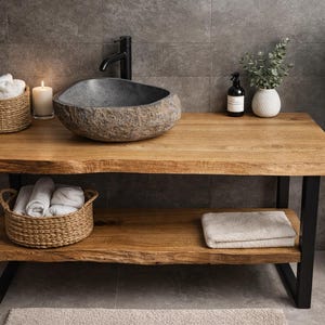 Pode incluir: Uma bancada de casa de banho rústica com um tampo de madeira natural e uma pia de pedra. A bancada tem uma prateleira inferior e pernas de metal preto. Cestos de vime contêm toalhas brancas enroladas e uma vela acesa adiciona ambiente.