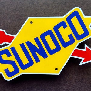 May include: A yellow diamond-shaped sign with a white border and two red arrows. The sign says "SUNOCO" in blue letters.