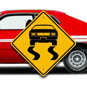 May include: A diamond-shaped yellow road sign featuring a black graphic of the rear view of a muscle car with two black tire skid marks underneath, positioned in front of a red car with white side stripes.