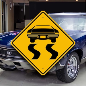 May include: Yellow diamond-shaped road sign with a black silhouette of a car driving on a winding road. The sign has a black border and a hole at the top for hanging. The sign is in front of a blue car with the word "SS" on the front.