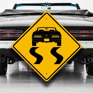 May include: Yellow diamond-shaped road sign with black silhouette of a car driving on a winding road. The sign reads "SS" in black.