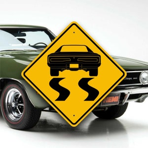 May include: A yellow diamond-shaped road sign with a black silhouette of a classic muscle car driving on a winding road. The sign reads "SS" in black lettering. The sign is in front of a green Dodge Charger.