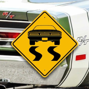 May include: A yellow diamond-shaped road sign with black lettering and a black silhouette of a car. The sign reads "SS" and depicts a car driving on a winding road.