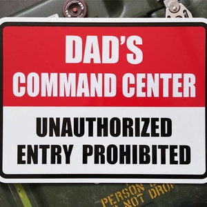 May include: White sign with black text that reads "Dad's Command Center Unauthorized Entry Prohibited". The sign has a red background at the top.