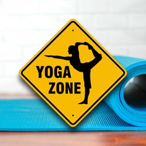 May include: Yellow diamond-shaped sign with black text and a silhouette of a person doing yoga. The sign reads "Yoga Zone".