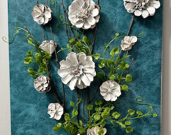 Può includere: Un'opera d'arte da parete decorativa con un bouquet di fiori di pigna bianchi e fogliame verde su uno sfondo strutturato color verde acqua. Il bouquet è legato con spago e steli di legno. Un'arrangiamento floreale unico.