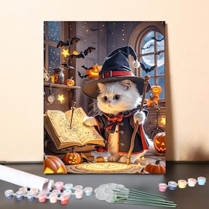 May include: A paint-by-number kit featuring a white kitten wearing a black witch hat and cape, holding a wooden staff. The kitten stands before an open spellbook with circular diagrams, surrounded by orange jack-o'-lanterns and flying bats.