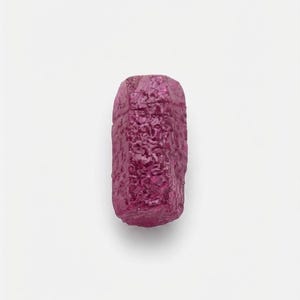May include: A raw, unpolished ruby crystal with a deep magenta-pink hue. The gemstone features a hexagonal, elongated columnar shape with a rough, textured surface showing natural crystalline facets and irregular edges throughout its structure.
