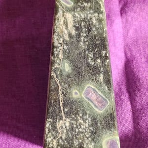May include: A green and purple crystal point with white flecks and a rough texture.
