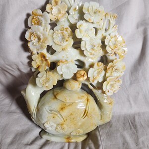 Peut inclure: Une sculpture en jade sculptée à la main d'une théière avec un arbre en fleurs qui pousse du haut. La théière et l'arbre sont de couleur vert pâle avec des accents bruns.
