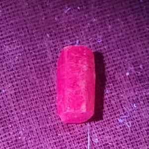 Peut inclure: Un objet cylindrique rose vif aux extrémités arrondies. Il est posé sur un tissu violet texturé. L'objet semble être solide. L'éclairage crée des reflets et des ombres sur sa surface.