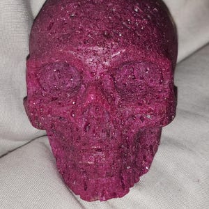 May include: A purple skull-shaped candle with a textured surface.