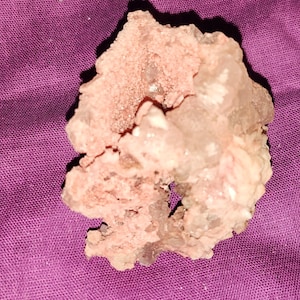 May include: A close-up of a pink and white mineral specimen. The mineral has a rough, textured surface with crystalline formations. The color is a mix of pale pink and translucent white, with some darker spots.