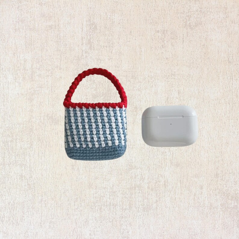 May include: A small blue and white striped crocheted bag with a red handle. The bag is next to a white AirPod case.
