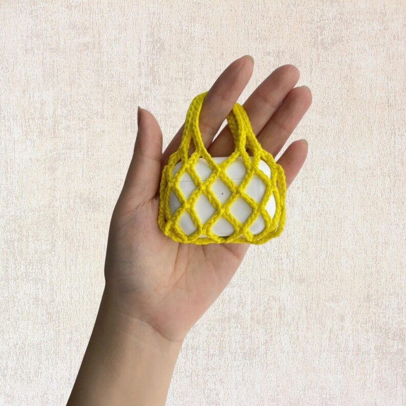 May include: A small yellow crocheted bag with a mesh design. The bag is being held in a hand.