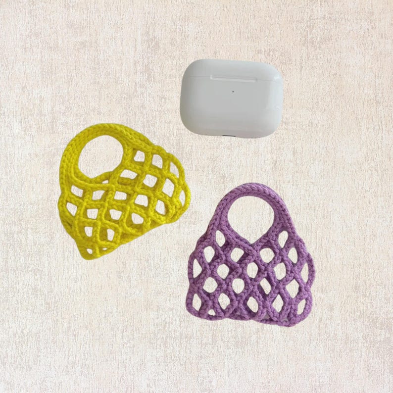 May include: Two small crocheted bags, one yellow and one purple, with a white rectangular case in the background.