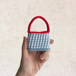 May include: A small crocheted handbag with a blue and white checkered pattern and a red handle.