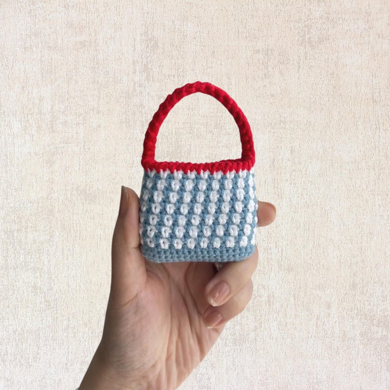 May include: A small crocheted handbag with a blue and white checkered pattern and a red handle.