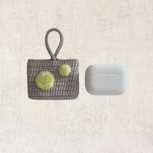 May include: A gray crocheted case with a loop handle and two yellow tennis ball embellishments. The case is next to a white AirPod case.