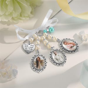 Può includere: Una collezione di ciondoli fotografici con perle, un nastro bianco e un ciondolo a forma di cuore. I ciondoli presentano cornici ovali con foto di persone. Il ciondolo a forma di cuore ha il testo "you are always in my heart!"