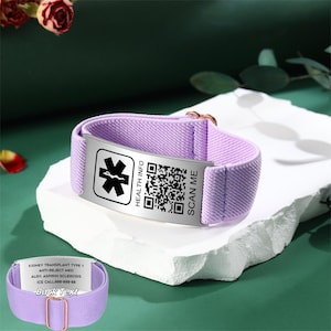 Könnte beinhalten: Ein lilafarbenes medizinisches Armband mit einer Metallplatte, die ein medizinisches Symbol, einen QR-Code und den Text "HEALTH INFO" und "SCAN ME" zeigt. Auf der Rückseite des Armbands steht "KIDNEY TRANSPLANT TYPE 1" und weitere medizinische Informationen.