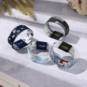 May include: Four fabric bracelets with various patterns. One bracelet features a navy blue background with white seashells and starfish. Another has a black and gray geometric design. The third has a blue floral pattern, and the fourth has a blue and white illustration.