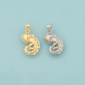 Peut inclure: Deux pendentifs caméléon, l'un doré et l'autre argenté, sont présentés sur un fond bleu clair. Les pendentifs présentent des queues enroulées et des corps texturés, sur le thème des reptiles. Ces pendentifs sont conçus pour les bijoux.