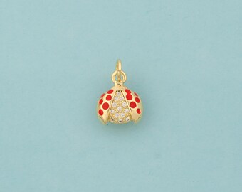 May include: A gold-colored ladybug charm with red spots and a crystal-studded lower half. The charm has a loop at the top for attaching to a necklace or bracelet. The background is a solid light blue.
