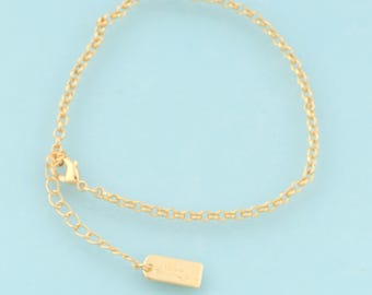 May include: A gold chain bracelet with a small tag charm. The tag has an inscription on it.