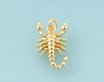 Puede incluir: Un dije de escorpión dorado con patas, pinzas y cola curvada detalladas. El dije tiene un lazo en la parte superior para sujetarlo a un collar o pulsera. El escorpión está sobre un fondo azul claro.
